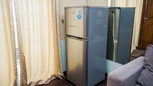 A compact, two-door refrigerator in a room with a wooden floor and a patterned curtain. - Fully Furnished 2BR Apartment at Great Western Resort (Tangerang)