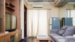 A living room with a television on a wooden cabinet, a grey sofa, and a small wooden table. - Fully Furnished 2BR Apartment at Great Western Resort (Tangerang)
