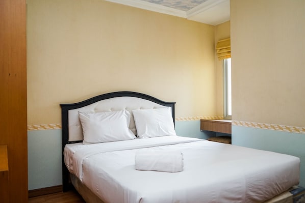 A neatly made bed with white linens and pillows, a wooden headboard, and a window with yellow curtains.
