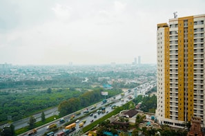 A high-rise building with multiple floors, surrounded by greenery and a busy road with vehicles.