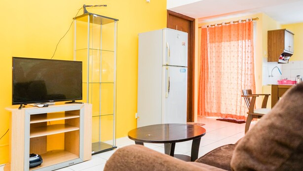 A living room with a TV, a glass cabinet, a refrigerator, and a dining area with a table and chairs. - Comfy and Cozy 2BR Great Western Resort Apartment (Tangerang)