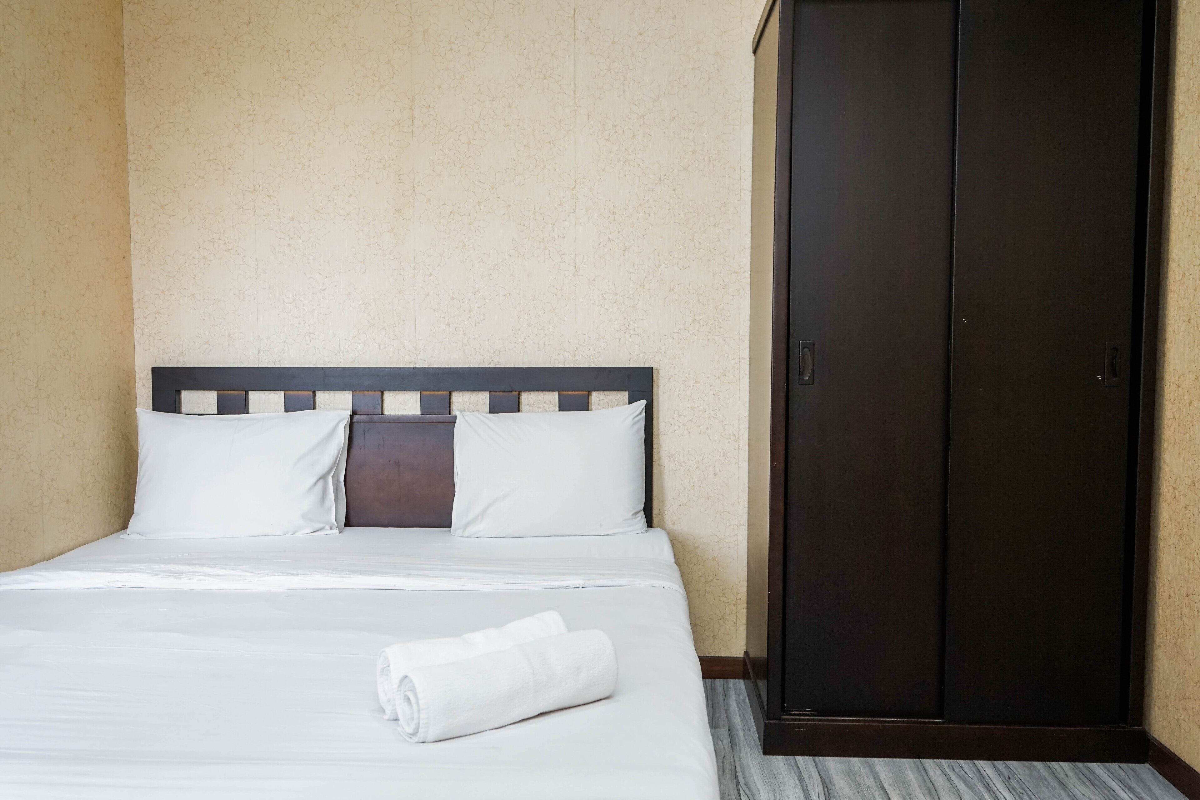 Een hotelkamer met een bed, een donkere houten garderobe en een eenvoudige wand.