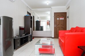 Ein Wohnzimmer mit Glastisch, rotem Sofa, Fernseher und Schrank.