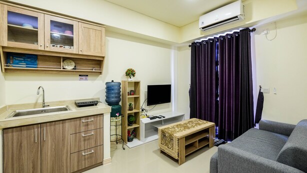 A compact living space with a kitchenette, a flat-screen TV, a sofa, and a water dispenser. - New Furnished and Comfy 2BR at Meikarta Apartment (Cikarang)