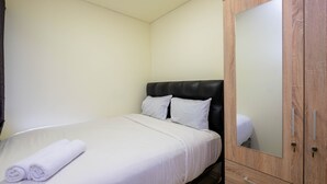 A neatly made bed with white linens and rolled towels, a wooden wardrobe with a mirror, and a plain wall. - New Furnished and Comfy 2BR at Meikarta Apartment (Cikarang)