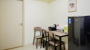 A small kitchenette with a refrigerator, a coffee maker, and a microwave. There are four wooden chairs and a table. - New Furnished and Comfy 2BR at Meikarta Apartment (Cikarang)