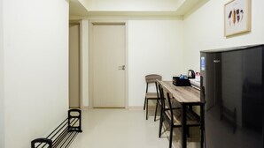 A compact room with a dining table, chairs, a refrigerator, and a door leading to another room. - New Furnished and Comfy 2BR at Meikarta Apartment (Cikarang)