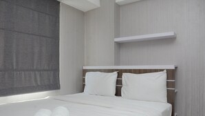 Ein ordentlich bezogenes Bett mit weißen Leinen und Kissen, ein grauer Vorhang und ein weißes Regal an der Wand.