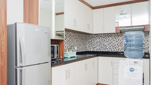 Eine kleine Küche mit weißen Schränken, einem Edelstahlkühlschrank, einem Wasserspender und einer gefliesten Spritzschutzwand.