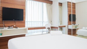Ein modernes Hotelzimmer mit einem großen Bett, einem Schreibtisch, einem Sessel, einem Fernseher und einem Spiegel.