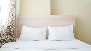 Un lit avec deux oreillers blancs et une tête de lit sobre, dans une pièce aux murs unis et ornée d’un rideau à motifs géométriques.