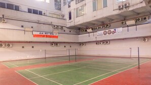 Un court de tennis intérieur comprenant plusieurs terrains, des unités de climatisation et un panneau publicitaire annonçant la location d’une suite.