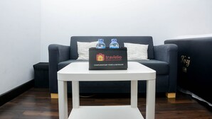 Une pièce avec un canapé bleu foncé, une table blanche sur laquelle se trouve un sac noir portant l’inscription « Travelio Property Management – produits alimentaires et boissons offerts », et deux bouteilles d’eau posées sur la table.