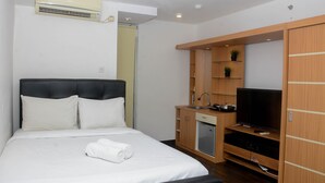 Une chambre avec un lit, un téléviseur encastré, une petite kitchenette et une armoire.