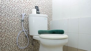 Une salle de bain équipée de toilettes, d’un flexible de douche et d’un mur carrelé.