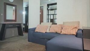 Una sala moderna con un sofá azul oscuro, almohadas a rayas, un escritorio con cajones, un reloj en la pared y una estantería.