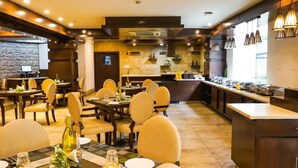 Un restaurante con varias mesas y sillas, una zona de cocina e iluminación colgante.