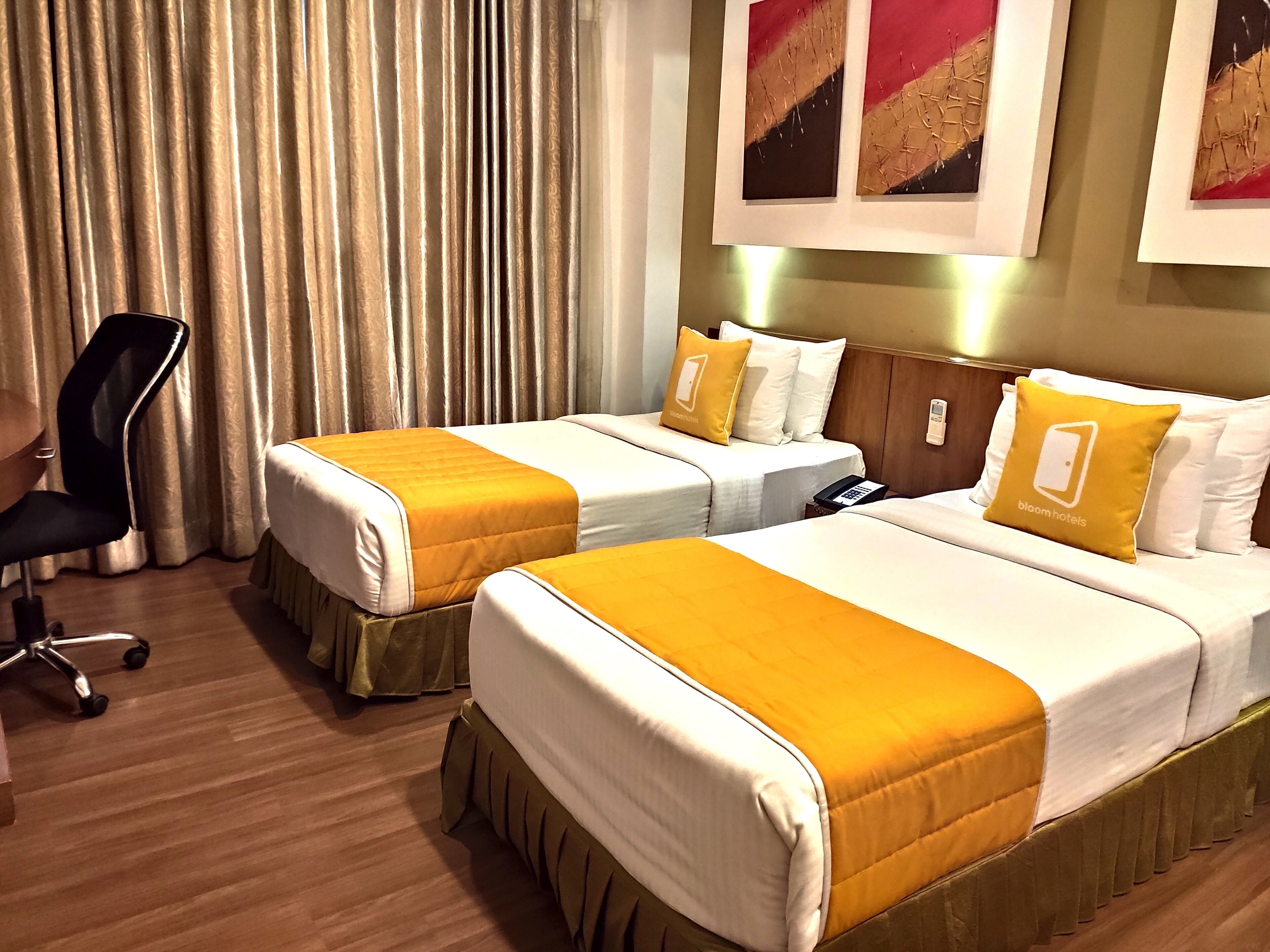 A hotel room with two beds, a desk, a chair, and a telephone.