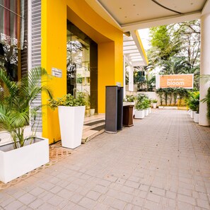 A hotel entrance with a yellow facade, potted plants, and a sign reading "INDIA IS IN FULL BLOOM".