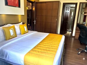 A hotel room with a bed, two pillows, a wooden wardrobe, and a desk with a chair.