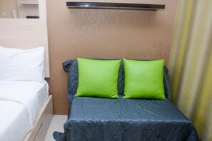 A bed with a grey quilt and two bright green pillows, a wooden headboard, and a beige wall. - Comfort and Spacious Studio Room Bassura City Apartment (Jakarta)