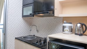A compact kitchen with a gas stove, a sink, a stainless steel range hood, and a kettle on the countertop. - Comfort and Spacious Studio Room Bassura City Apartment (Jakarta)