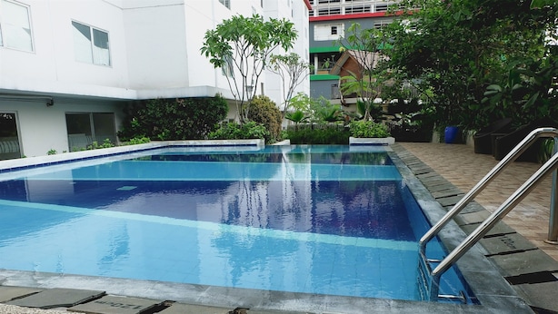 A rectangular swimming pool with a metal ladder on one side, surrounded by a pebble border. - Comfort and Spacious Studio Room Bassura City Apartment (Jakarta)