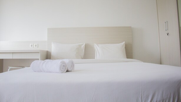 A neatly made bed with white linens and pillows, a white bedside table, and a closed wardrobe. - Comfort Studio Apartment at Urban Heights Residences (South Tangerang)