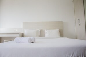 Een netjes opgemaakt bed met witte lakens en kussens, een witte nachtkastje en een gesloten garderobe.