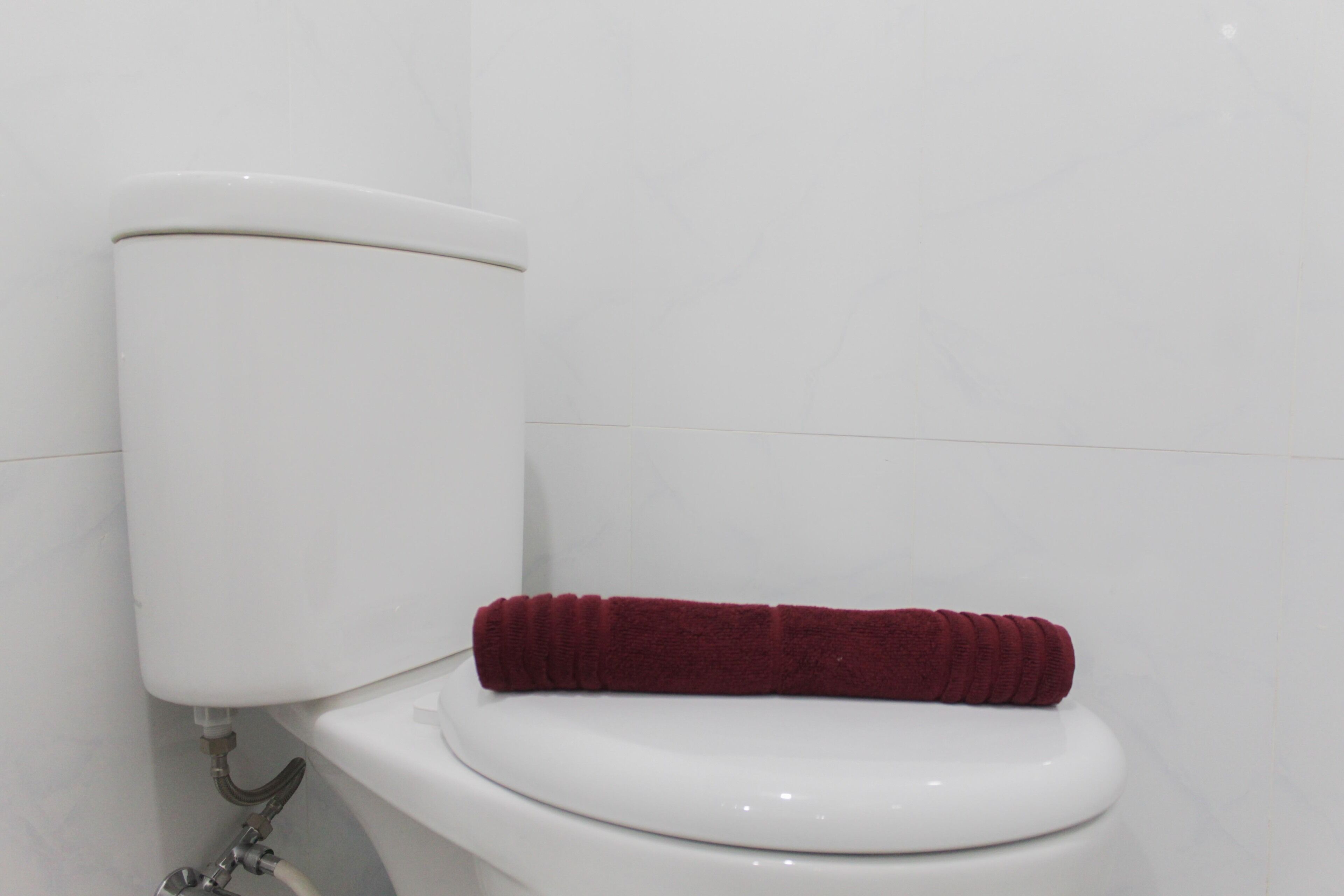 A toilet with a white tank and a red towel placed on the seat.