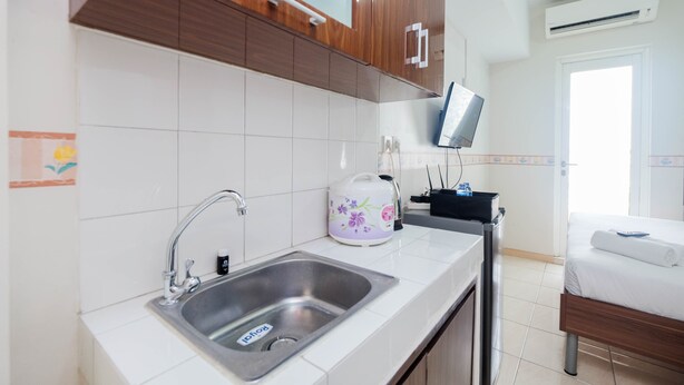 A modern kitchen with a stainless steel sink, wooden cabinets, and a flat-screen TV mounted above the counter. - Comfortable Studio at Springlake Summarecon Bekasi Apartment (Bekasi)