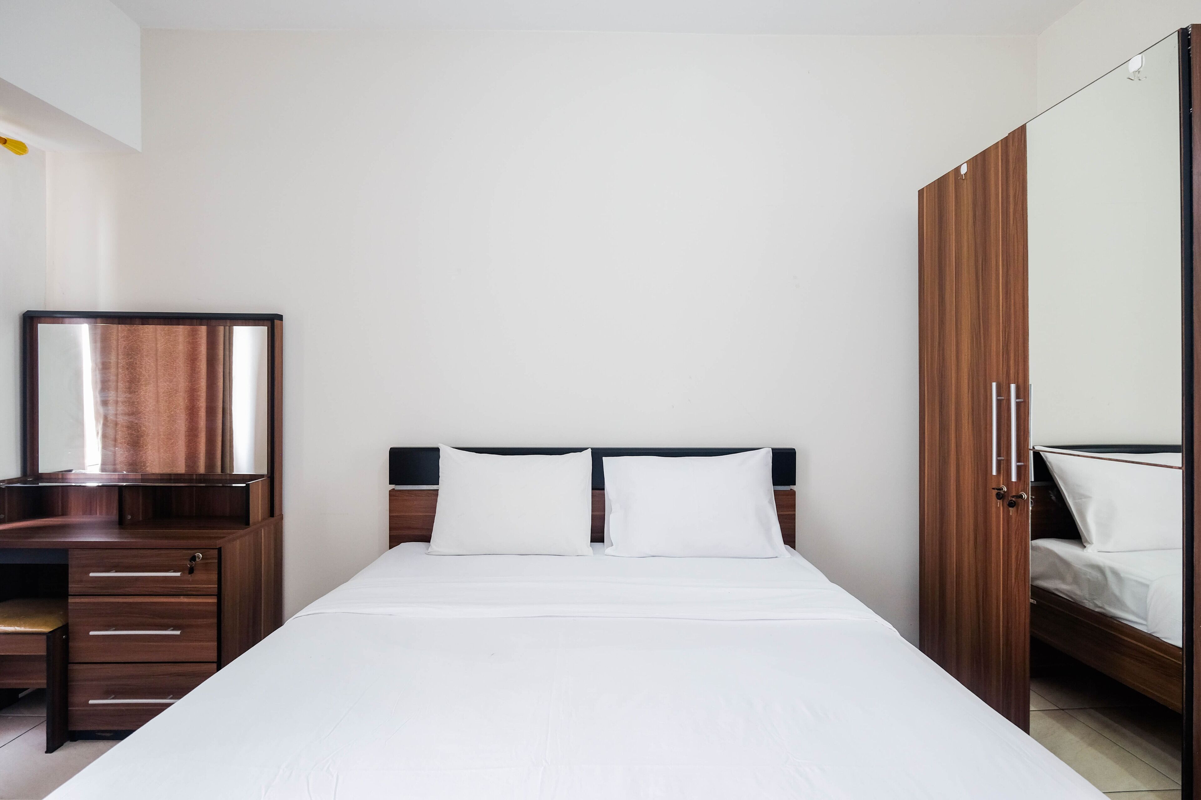 A bedroom with a wooden bed, two white pillows, a wooden dresser with drawers, and a mirror.