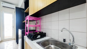 A kitchen with a stainless steel sink, a black stove, and a pink drying rack. - Comfortable Springlake Summarecon Studio Apartment near Mall (Bekasi)