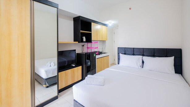 A hotel room with a bed, a TV, a desk with a computer, a mirror, and a wardrobe. - Comfortable Springlake Summarecon Studio Apartment near Mall (Bekasi)