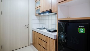 A compact kitchen with wooden cabinets, a stainless steel sink, and a black refrigerator with a 'SHARP' logo. - Comfort and Strategic Studio at Springlake Summarecon Bekasi Apartment (Bekasi)