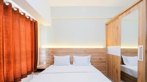 A modern hotel room with a wooden headboard, a large mirror, and a bed with white linens. - Comfort and Strategic Studio at Springlake Summarecon Bekasi Apartment (Bekasi)