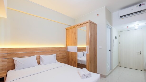A hotel room with a wooden headboard, a large mirror, a bed with white linens, and a wardrobe with a mirror. - Comfort and Strategic Studio at Springlake Summarecon Bekasi Apartment (Bekasi)
