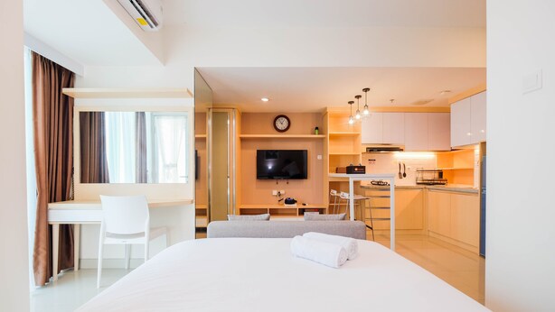 A hotel room with a bed, a desk, a chair, a TV, and a kitchenette. - Spacious Studio at Grand Kamala Lagoon Apartment (Bekasi)