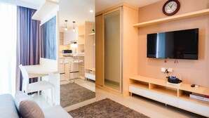 A modern living room with a sofa, a TV, a dining area with a table and chairs, and a kitchen in the background. - Spacious Studio at Grand Kamala Lagoon Apartment (Bekasi)
