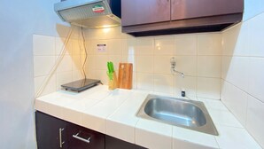 Une cuisine compacte avec des carreaux blancs, un évier en acier inoxydable, un four à micro-ondes et des ustensiles de cuisine en bois posés sur le plan de travail.