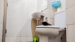 A bathroom with a toilet, a sink, and a green cleaning brush.