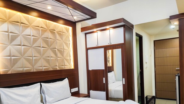 A hotel room with a large bed, a wooden headboard, a wardrobe with a mirror, and a door leading to a bathroom.