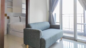 A modern bedroom with a bed, a grey sofa, and a large window with curtains. - Homey and Comfy 2BR at Vida View Apartment (Makassar)