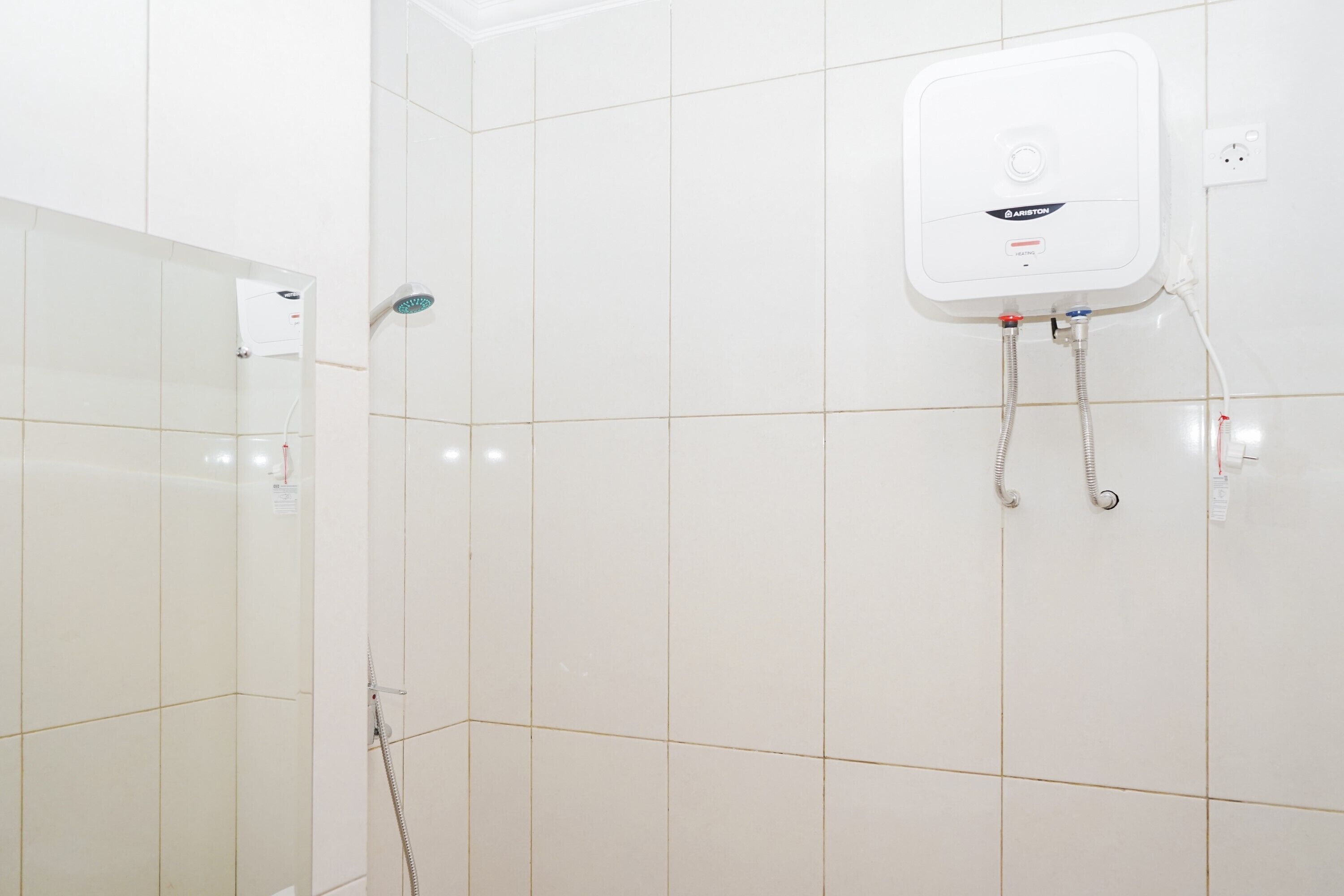 A bathroom with white tiled walls, a shower with a handheld showerhead, and a wall-mounted water heater.