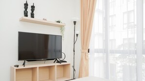 Una sala de estar moderna con un televisor de pantalla plana sobre un soporte de madera, una lámpara de pie y una ventana con cortinas traslúcidas.