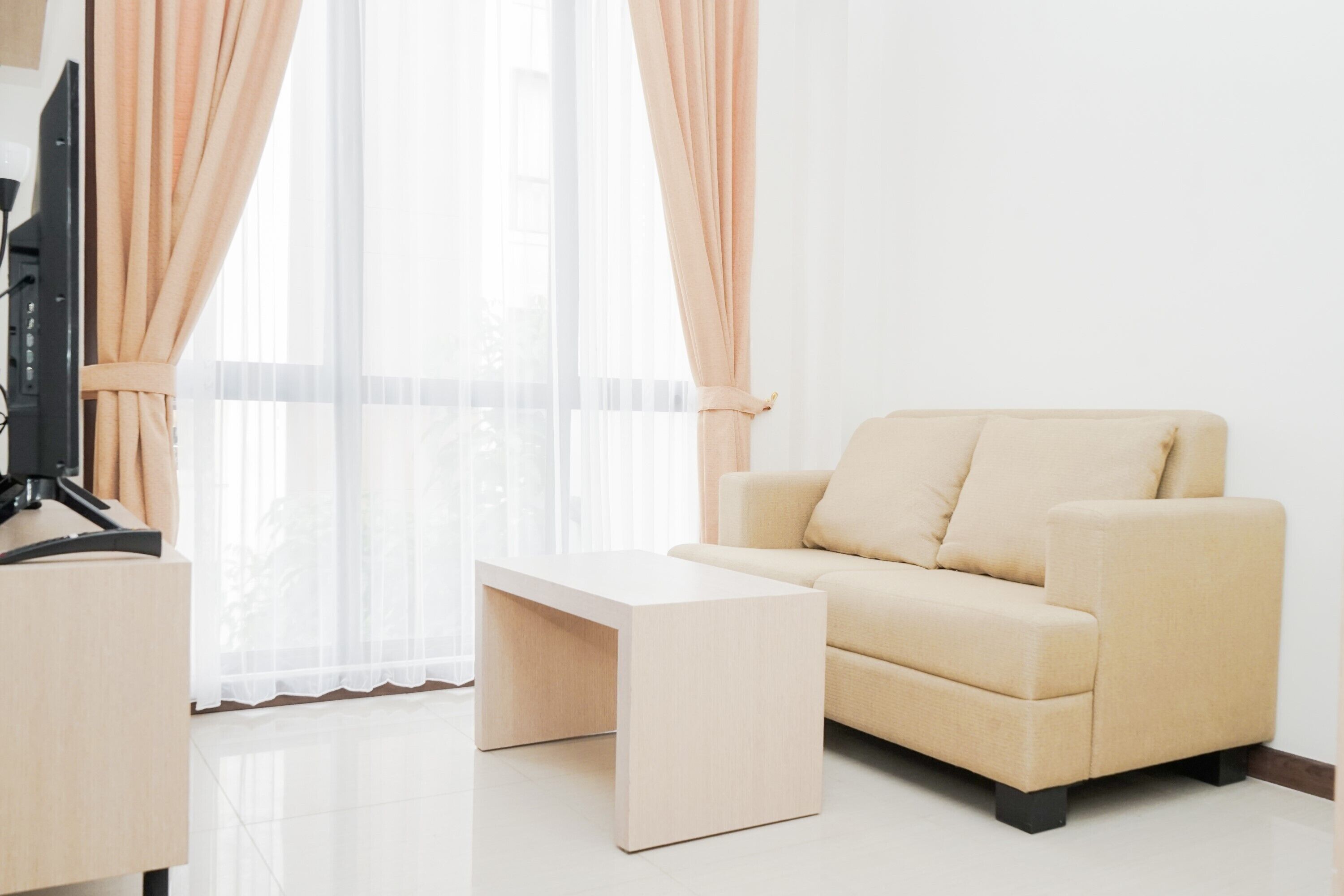 Una sala de estar moderna con un sofá color beige, una mesa de centro blanca y un televisor de pantalla plana sobre un soporte.