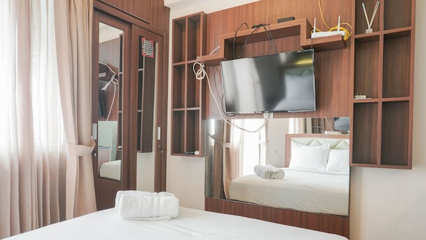 Une chambre d’hôtel avec un lit, un téléviseur fixé au mur, un miroir et une étagère en bois sur laquelle se trouve un autre téléviseur.