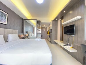 A modern hotel room with a large bed, a TV mounted on the wall, and a kitchen area visible through an open door. - Luxurious Studio Room at Galeri Ciumbuleuit 3 near UNPAR (Bandung)