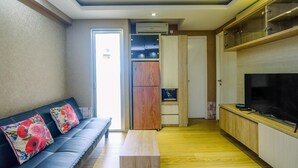 A modern living room with a sofa, a coffee table, a TV, and built-in cabinets. - Modern 2BR at Bassura City Apartment (Jakarta)