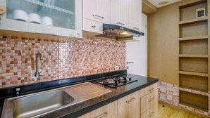 A kitchen with a tiled backsplash, stainless steel sink, and wooden cabinets. - Modern 2BR at Bassura City Apartment (Jakarta)